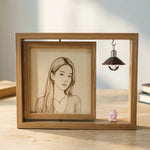 Shadow box frame with hand-drawn portrait, hanging miniature lamp and pig figurine on desktop