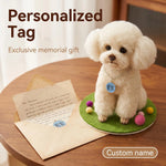 A small white fluffy dog figurine wearing a personalized blue circular tag sits on a green felt base with colorful pom-poms on a wooden table. An open letter and matching card are placed beside it, with the text 'Personalized Tag' and 'Exclusive memorial gift' above, plus a 'Custom name' label at the bottom right.