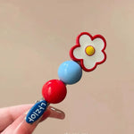 Single daisy flower clip with cherry red and blue beads held in hand