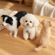 Three handmade wool felt pet replica figurines on a light wood tabletop. Black and white border collie, white poodle with personalized name tag, light tan dog facing away, custom handmade pet portrait gift.